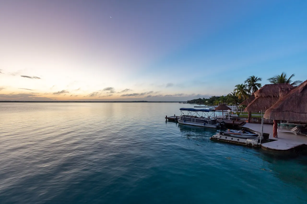Bacalar Lagoon with turquoise water, a wooden dock, boats and palm trees on the shore