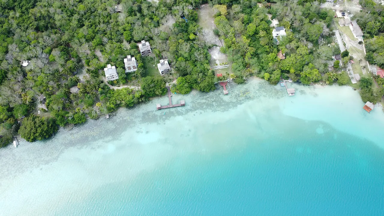 Aerial view of the Bacalar lagoon shore with bands of white, turquoise and blue water