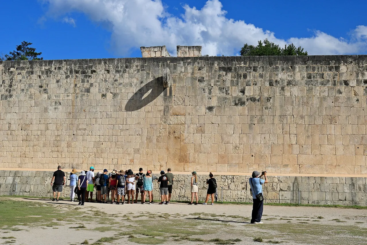 Stone ring high on the wall of Chichen Itza's Great Ball Court with a group of visitors below