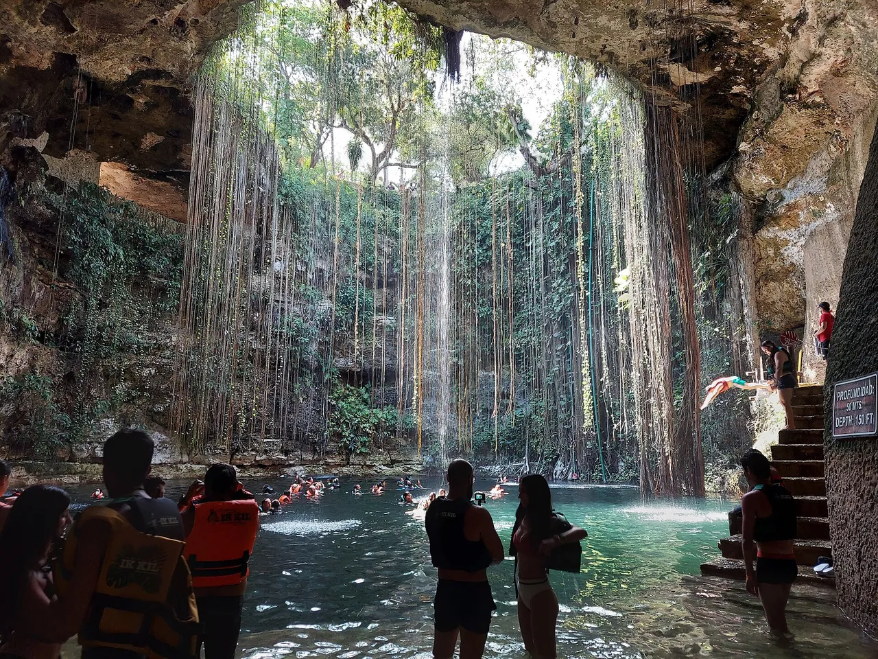 Ik Kil cenote seen from above, with hanging roots and swimmers in life jackets