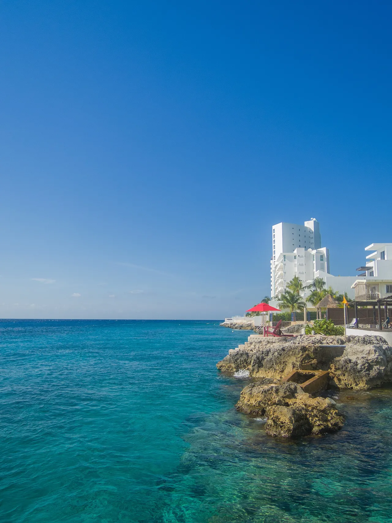 Clear turquoise water beside a rocky shore with a hotel on Cozumel's west coast