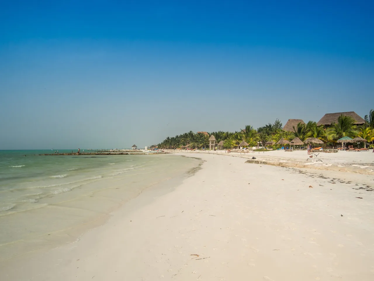 White-sand beach on Holbox with clear shallow water, palm trees and palapas