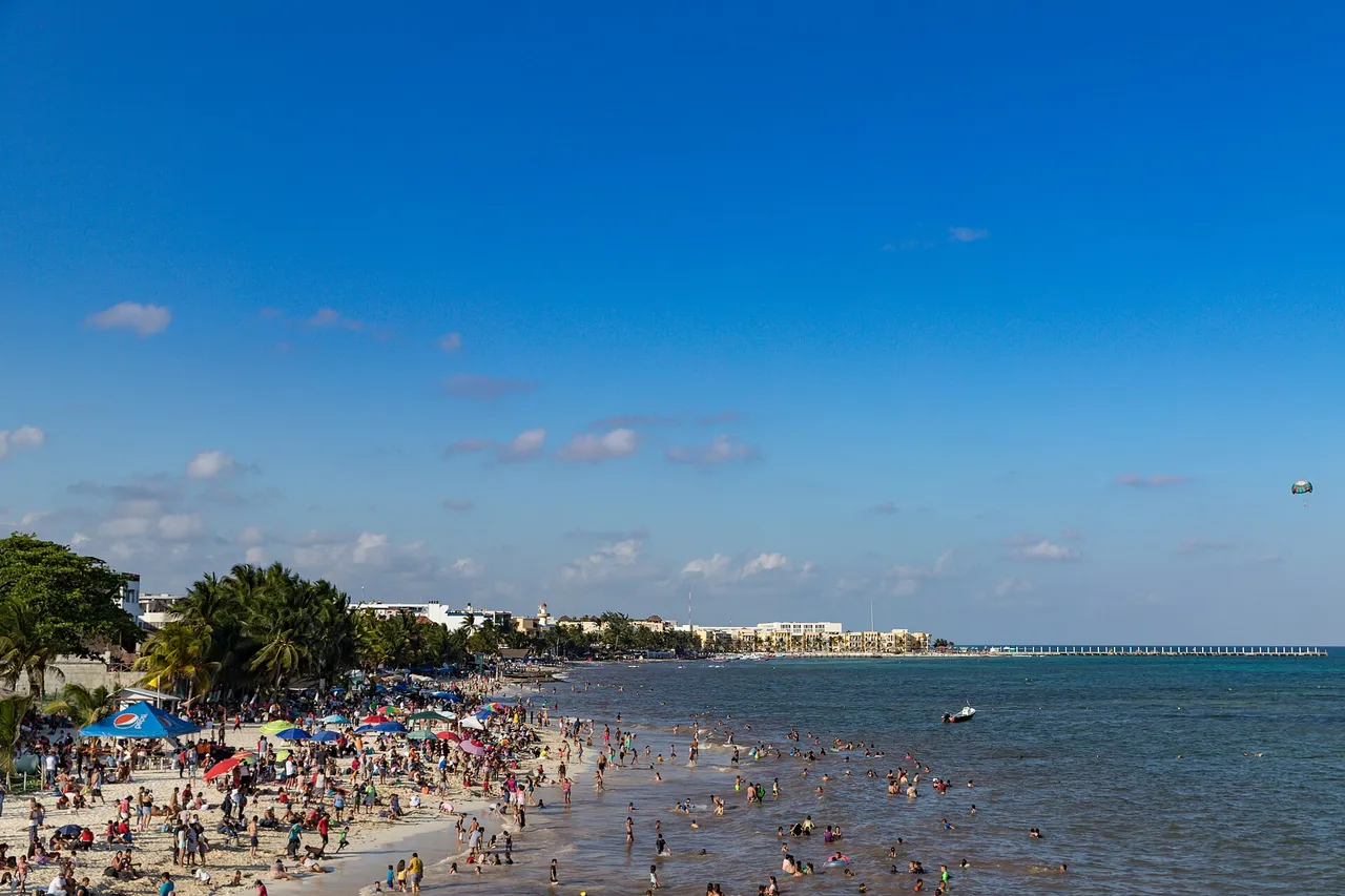 The town beach in Playa del Carmen with beachgoers on the sand and the pier in the background