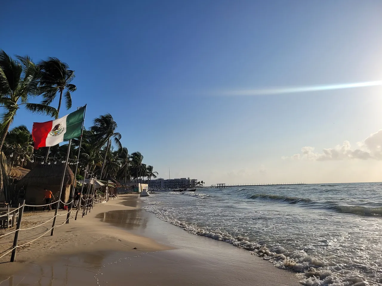Sunrise on a beach in Playa del Carmen with palm trees and a Mexican flag