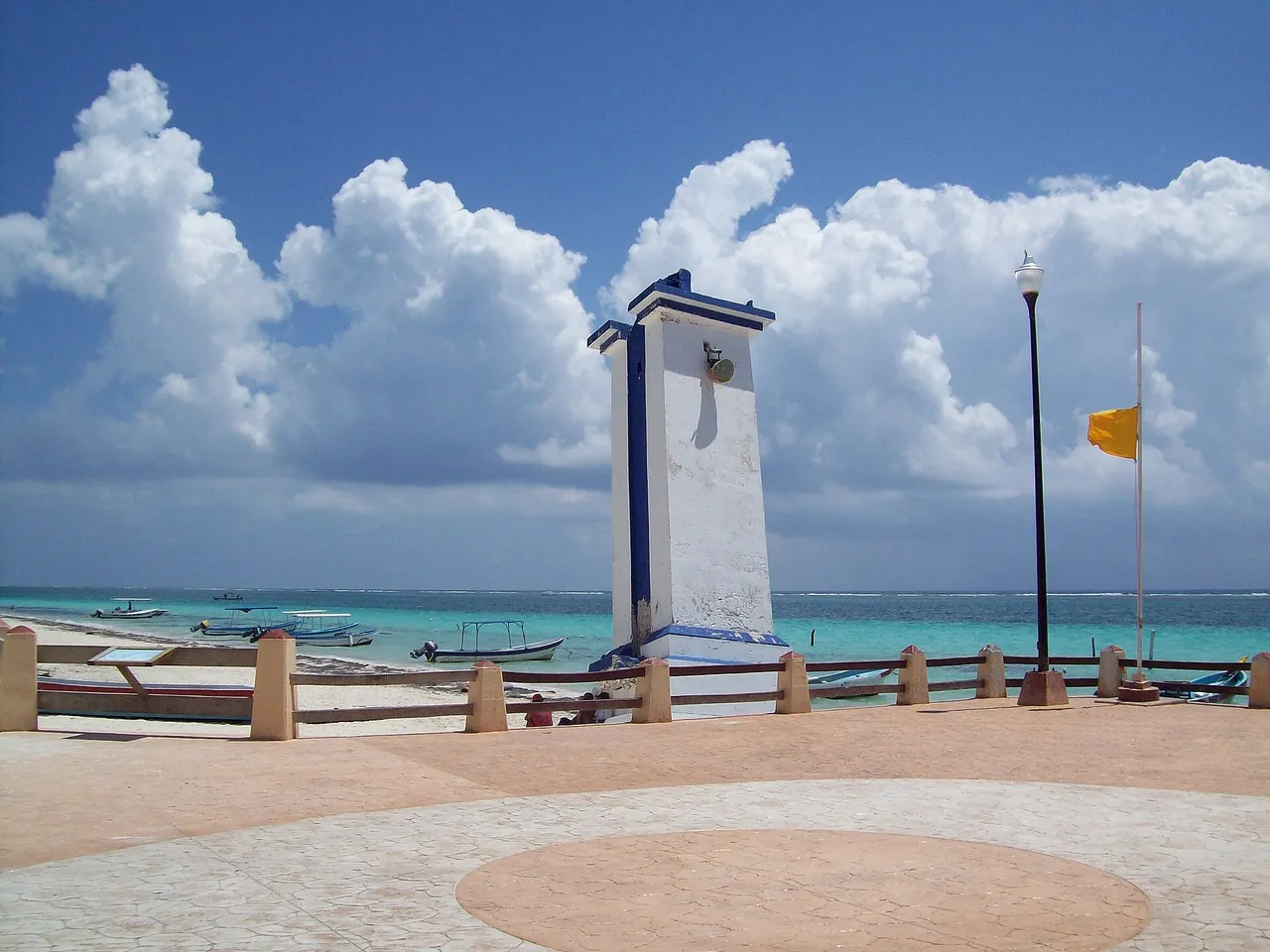 Puerto Morelos' leaning lighthouse beside the turquoise reef lagoon, with boats at anchor