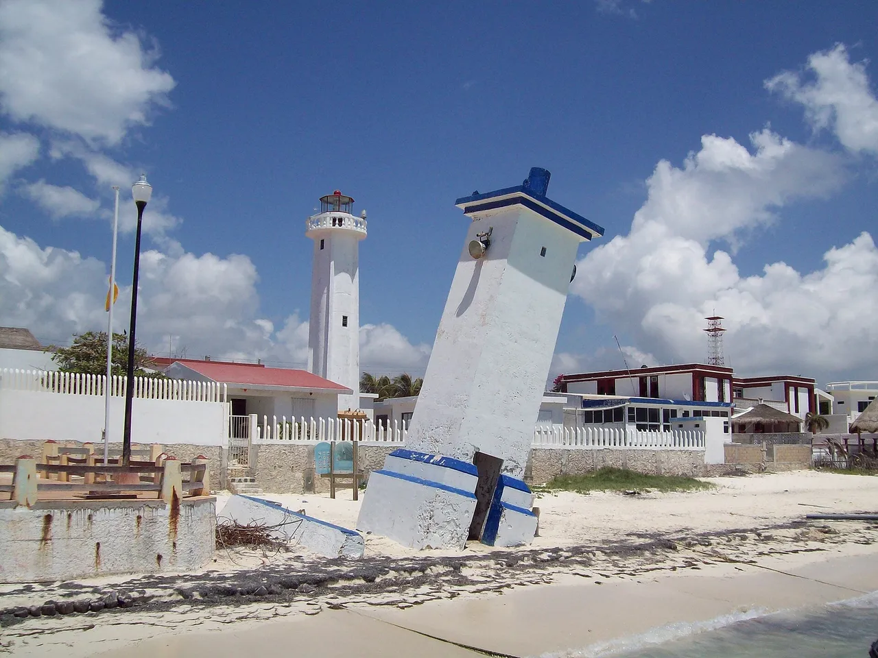 Leaning lighthouse of Puerto Morelos on the sand with the straight white newer lighthouse behind it