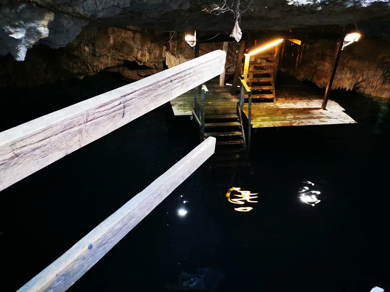 Dark interior of a cavern cenote with wooden stairs and a platform