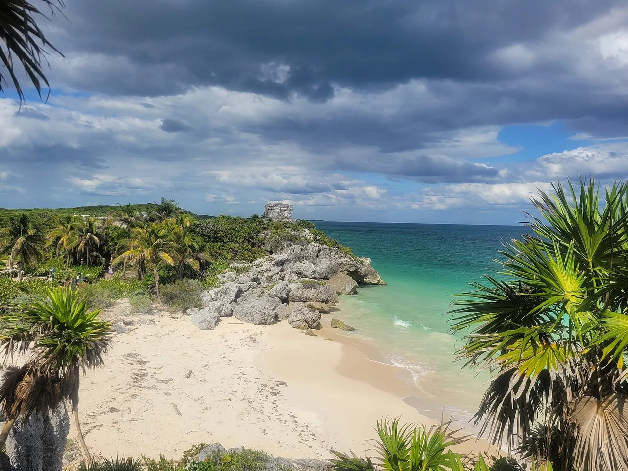 White-sand beach below the Tulum ruins, with the Temple of the Wind God on the rocks and a turquoise sea