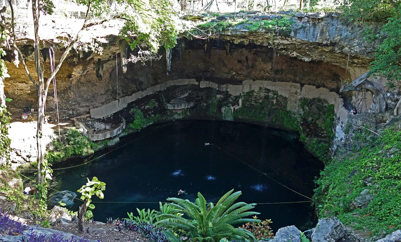 Zací cenote in Valladolid seen from the rim, with dark green water under a rock overhang and vegetation