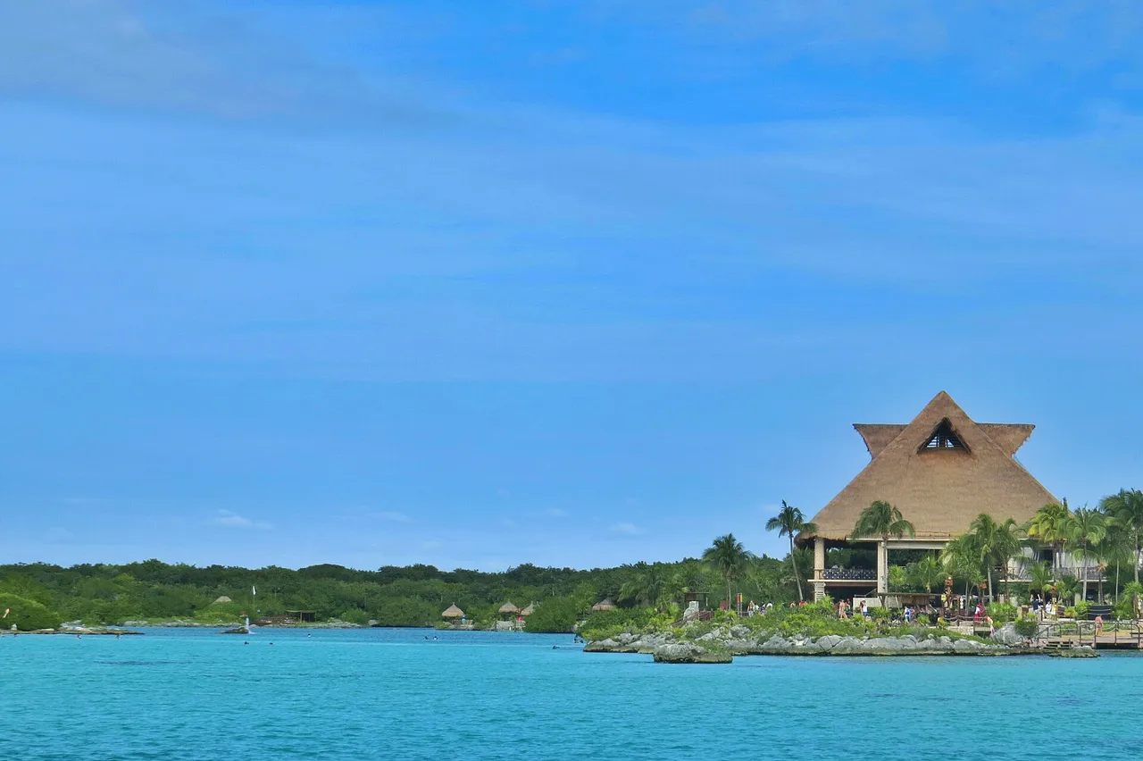 The Xel-Há inlet with green-turquoise water and a large palapa-roofed building on the shore
