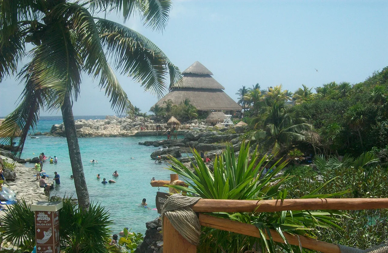 Beach and inlet inside Xcaret park with a palapa roof and palm trees